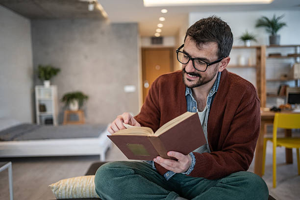 istock Young man reading a book at home and smiling 2223527286