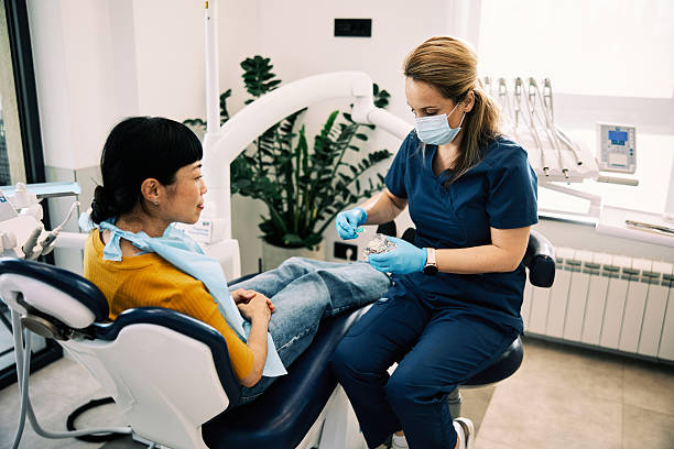 Japanese Woman Receiving Dental Care in Modern Clinic A Japanese woman sits in a dental chair while a female dentist in blue scrubs and mask prepares tools in a bright, modern clinic. dental care stock pictures, royalty-free photos & images
