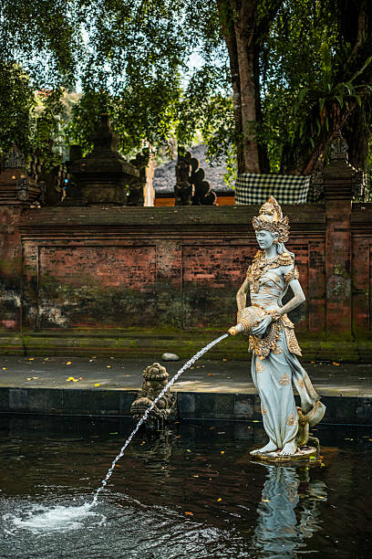 Statue of the Dedari pouring water into a temple pond in Bali, symbolizing divine beauty and spiritual purification. Pura Tirta Empul. Bali, Indonesia.