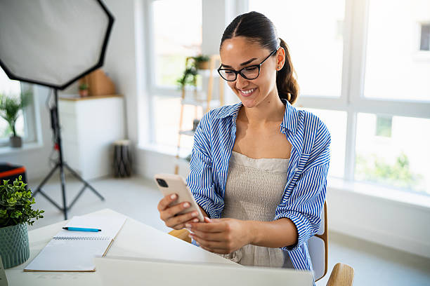 istock Smiling young female photographer working on a cellphone in a bright modern office setting 2223531574