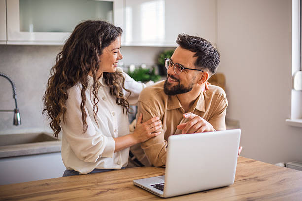 istock Young couple smiling and using laptop in kitchen 2223536509
