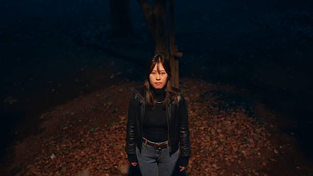 A Portrait of a woman standing under warm colored street light and looking at the sky in the evening in a public park.