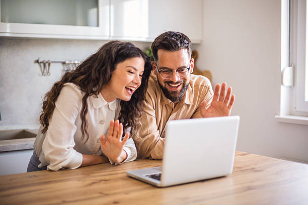 istock Happy couple video calling and waving at someone using laptop in kitchen 2223536735