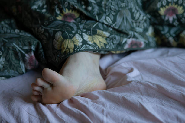 istock A persons feet are noticeably sticking out from underneath a blanket on a bed 2223536741