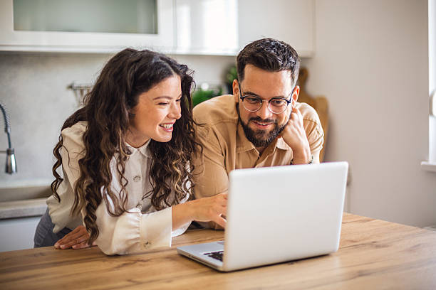 istock Young couple smiling and browsing internet on laptop in kitchen 2223536898