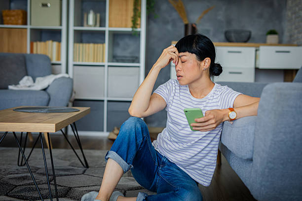 worried woman reading message on smartphone at home - イライラする ストックフォトと画像