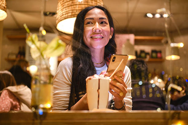 istock Smiling asian woman using mobile phone while having dessert in cafe 2223537210
