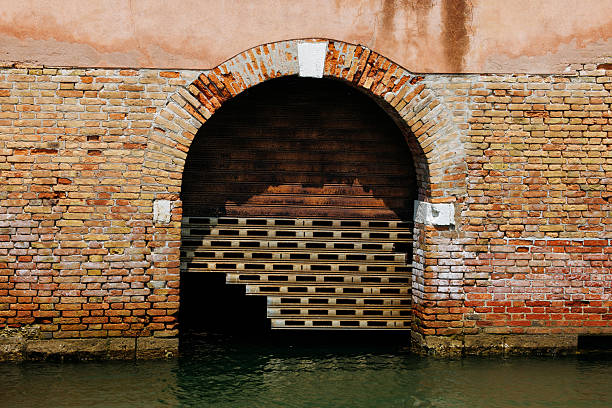 Brick archway over water with rustic gate in venetian setting, lifestyle concept