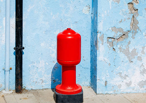 Red water pipe against weathered blue wall with exposed plaster details, lifestyle concept