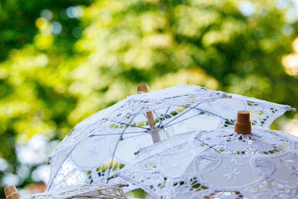 White lace parasols against vibrant green trees in sunlight, lifestyle concept