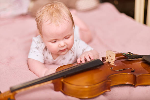 istock Curious baby girl with violin on soft pink bedding 2223542509