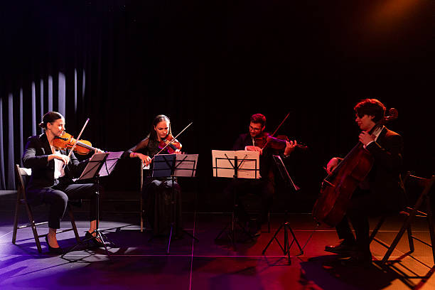 istock Four string quartet musicians play viola, cello and violins while sitting next to each other and performing classical music on a theater stage 2223543349