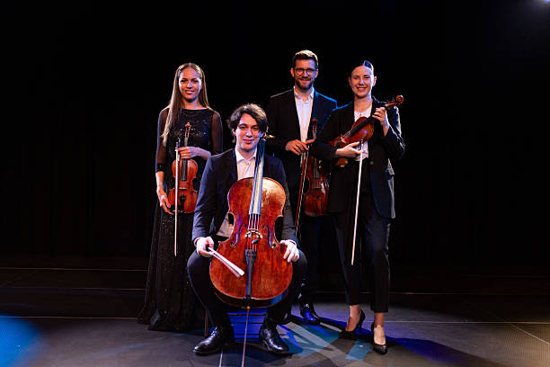 istock Portrait of a confident string quartet standing on stage under stage lights, holding instruments in hands and looking directly into camera 2223543410