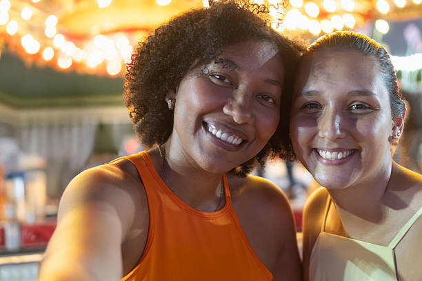 Two young adult women smiling and enjoying a vibrant, festive atmosphere with bright lights in the background