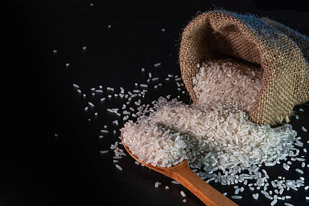 istock White rice spilling from a burlap sack onto a dark surface, with black background 2223548530
