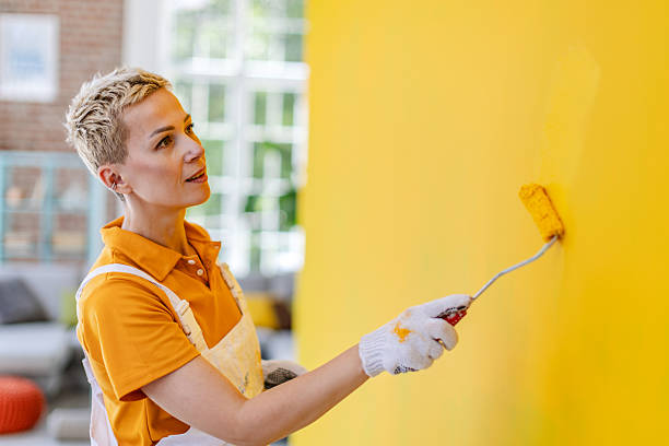 istock Female house painter refreshing interior wall with bright yellow paint in modern apartment setting 2223550097