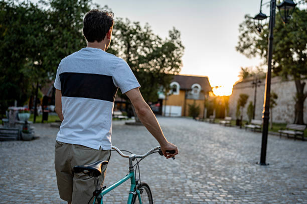 istock Man Walking a Bicycle in a Peaceful Urban Park at Sunset 2223550907