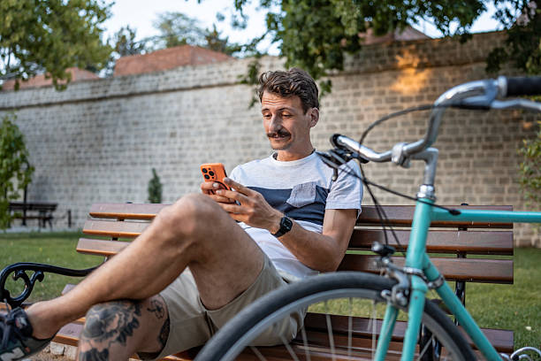 istock Man Relaxing on Bench Browsing Smartphone Outdoors Near Bicycle 2223550917
