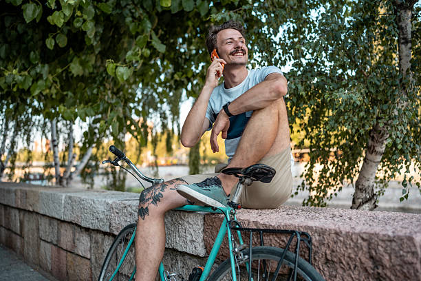 istock Smiling Man Talking on Phone While Relaxing With Bicycle Outdoors 2223551128
