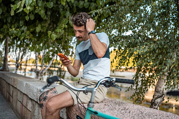 istock Man Checking His Smartphone While Sitting Outdoors Next to His Bicycle 2223551238