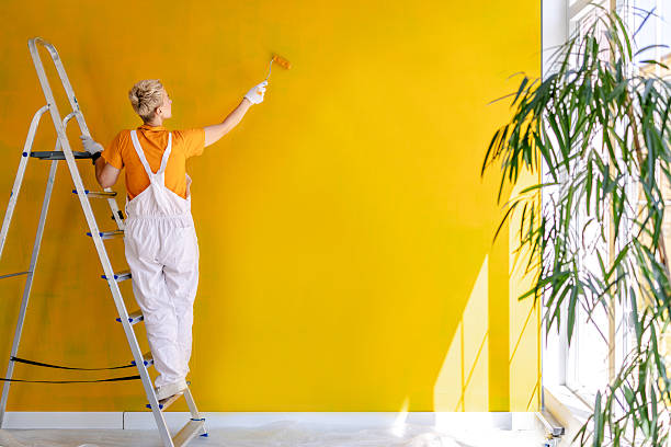 istock Female house painter decorating a bright yellow wall in an indoor space 2223551315