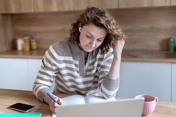 istock Enthusiastic woman student studying at home writing notes, listening online webinar wearing earbuds. 2223554873
