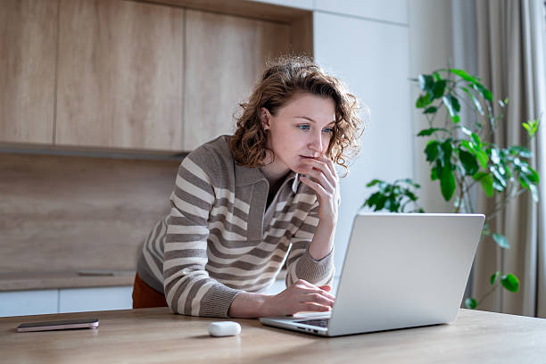 Serious concentrated young woman using laptop for remote work, research or online learning from home