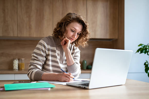 istock Thoughtful student woman taking online course with laptop concentrating on study materials at home. 2223555036