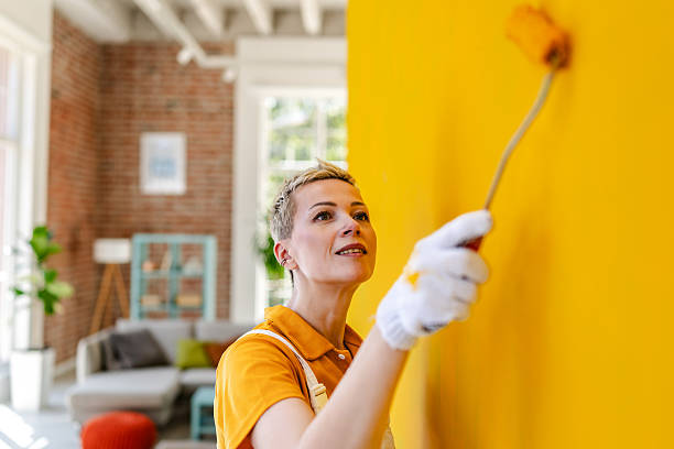 istock Female house painter working on a vibrant yellow wall in a modern home interior 2223555597