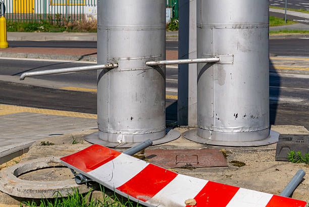 istock two vertical district heating pipes with metal support brackets, a fallen red-and-white warning sign at the base, and visible road and sidewalk infrastructure in the background. 2223556766