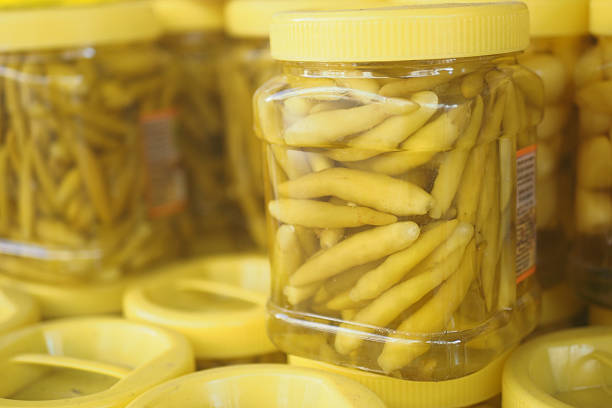 Jars filled with yellow pickled peppers are arranged for sale in a market.