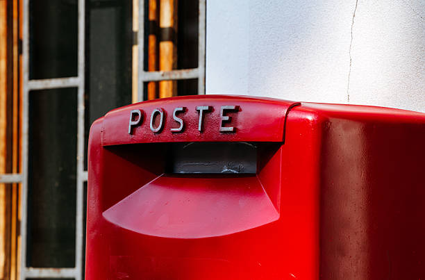 Burano, Italy - June 25, 2025: Red mailbox marked POSTE is positioned against a white wall, highlighting urban design and color vibrancy