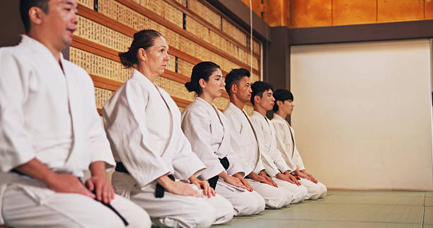 istock Discipline, kneeling and people in martial arts studio for practice, training or self defense class. Culture, karate and group of students with respect, honor or etiquette gesture to master in dojo. 2223560303