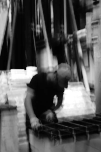 A highly out-of-focus image showing a person in dark clothing working near a metal structure, with the background completely blurred.