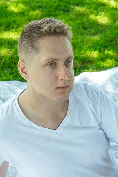 A young man sits thoughtfully in a beautiful park, surrounded by lush greenery, radiating calm and reflection