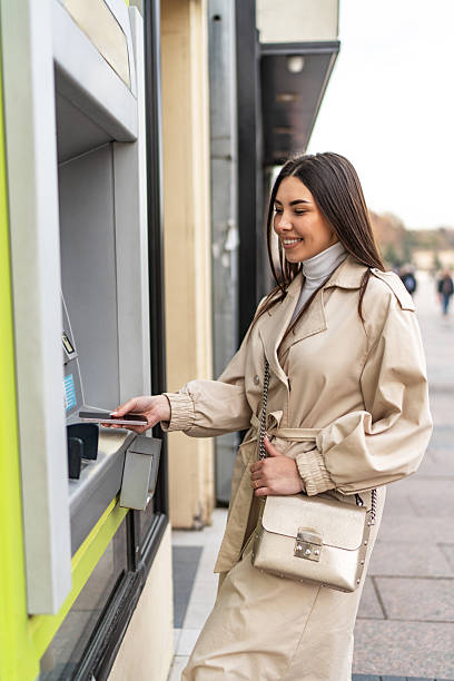 istock Young woman withdrawing cash from atm using mobile phone 2223571887