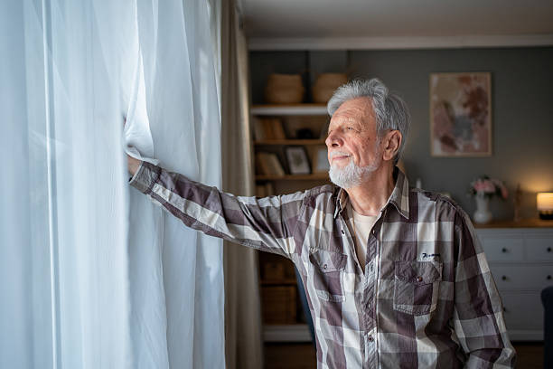 istock Senior man opening curtains and looking out the window 2223577136