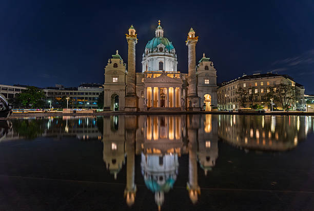 Night view of Karlskirche (St. Charles Church) in Vienna, Austria, beautifully illuminated with baroque columns and modern sculpture in the foreground.