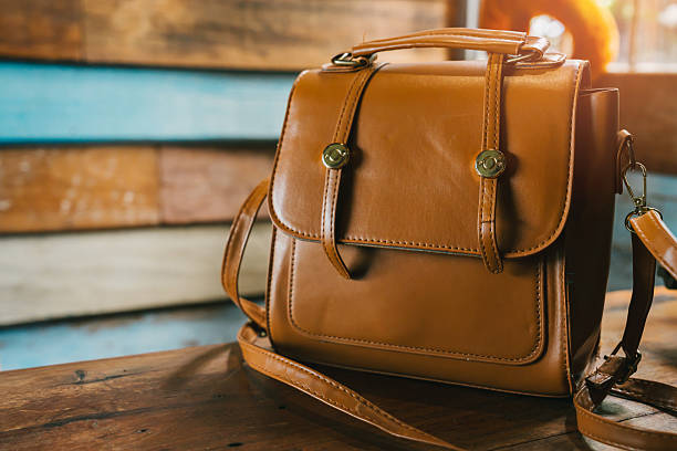 Stylish brown leather handbag on wooden table with rustic background and warm lighting for fashion and lifestyle themes.