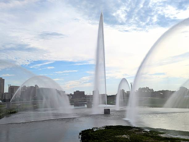 A long exposure photo of the Five Rivers Fountain in downtown Dayton Ohio just before sunset. Fountain is made up of giant water spouts that shoot water high up in the air over the river.  Photo is taken early June in the early evening.