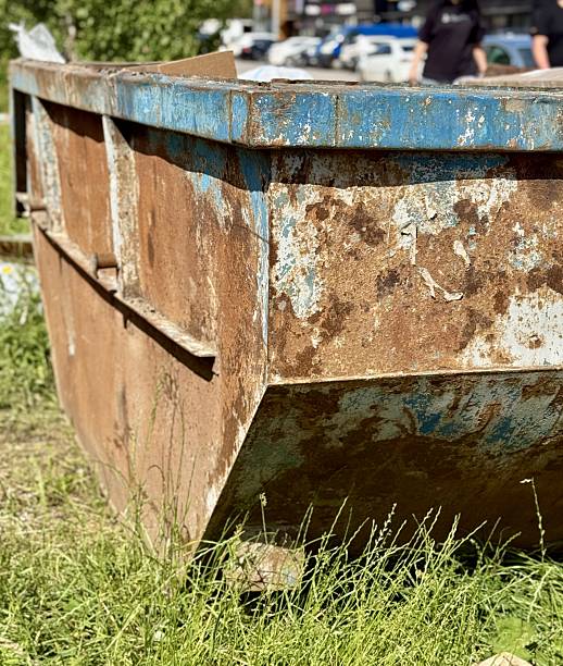 istock An Old and Rusty Dump Container That is Surrounded by Lush, Overgrown Grass and Weeds. A weathered metal dumpster overflowing with various debris, positioned against a backdrop of lush tall grass 2223607841