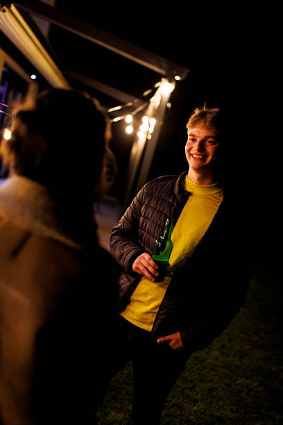 istock Young man enjoying an outdoor evening social gathering under string lights holding a beverage bottle. 2223610465