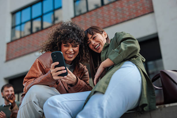 istock Two young women laughing while looking at smartphone screen outdoors 2223610619