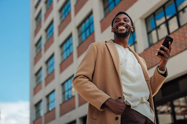 istock Young businessman smiling and using smartphone in front of office building 2223610628