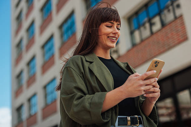 istock Young businesswoman smiling while using smartphone in front of office building 2223610632