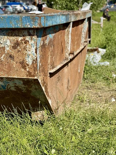 istock An Old and Rusty Dump Container That is Surrounded by Lush, Overgrown Grass and Weeds. A weathered metal dumpster overflowing with various debris, positioned against a backdrop of lush tall grass 2223611054