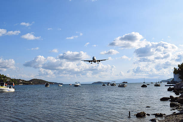 Commercial airplane coming in to land over the harbor at Skiathos International Airport, Greece. The low flying plane travels close to the water over small fishing boats. Bright summer's day in Greece