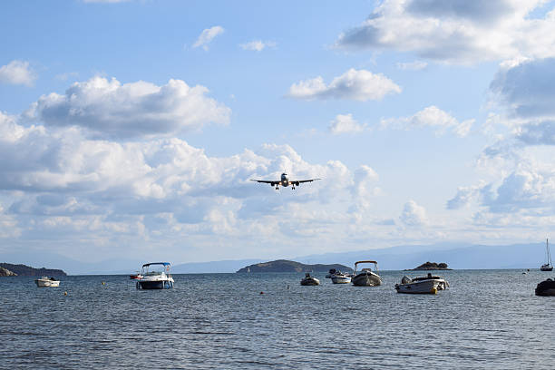 Commercial airplane coming in to land over the harbor at Skiathos International Airport, Greece. The low flying plane travels close to the water over small fishing boats. Bright summer's day in Greece