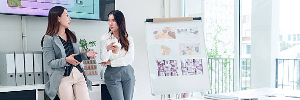 istock Two Asian Women Interior Designers Discussing Project Plans Near a Whiteboard in a Bright Studio, Showcasing Collaboration and Design Solutions 2223614411