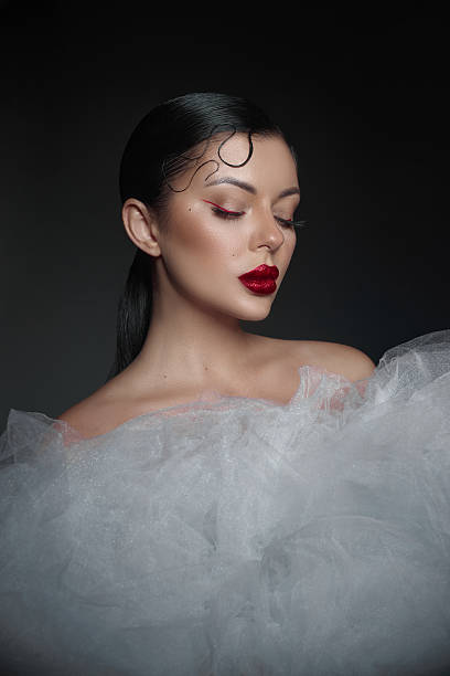istock model displays a sophisticated look with bold red lipstick and flawless makeup, wearing a voluminous tulle design that highlights her beauty in a professional studio setting 2223618085